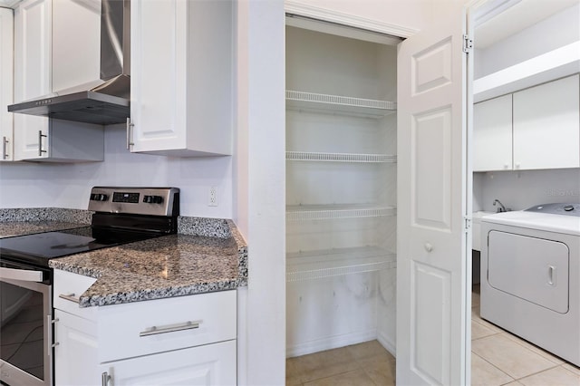 interior space featuring electric stove, wall chimney exhaust hood, light tile patterned floors, white cabinetry, and washer / clothes dryer