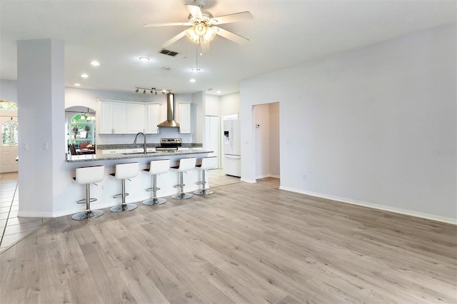 kitchen featuring kitchen peninsula, light hardwood / wood-style flooring, white cabinetry, white fridge with ice dispenser, and a breakfast bar area