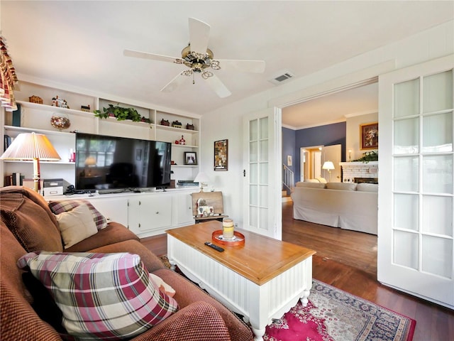 living room with dark hardwood / wood-style flooring, ornamental molding, built in shelves, ceiling fan, and a fireplace