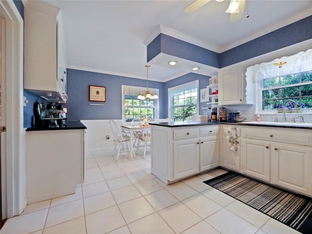 kitchen featuring white cabinetry, kitchen peninsula, pendant lighting, ceiling fan with notable chandelier, and ornamental molding