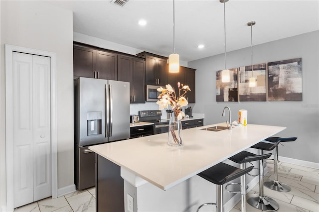 kitchen with a kitchen bar, appliances with stainless steel finishes, dark brown cabinetry, a center island with sink, and decorative light fixtures