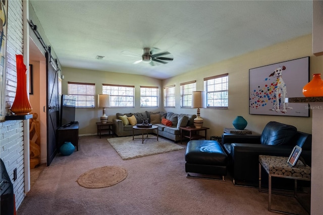 carpeted living room featuring ceiling fan, a barn door, a textured ceiling, vaulted ceiling, and a fireplace