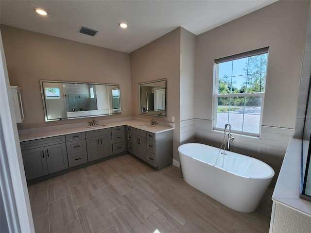 bathroom with a textured ceiling, vanity, separate shower and tub, and tile walls