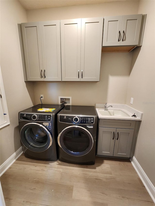 laundry area featuring washing machine and clothes dryer, light hardwood / wood-style flooring, cabinets, and sink