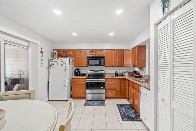 kitchen with light tile patterned floors, white appliances, light stone counters, and sink