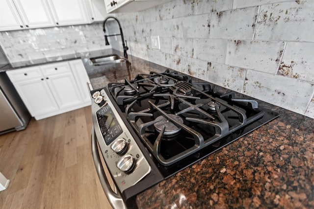 interior details with sink, black gas cooktop, light hardwood / wood-style flooring, dark stone countertops, and white cabinets