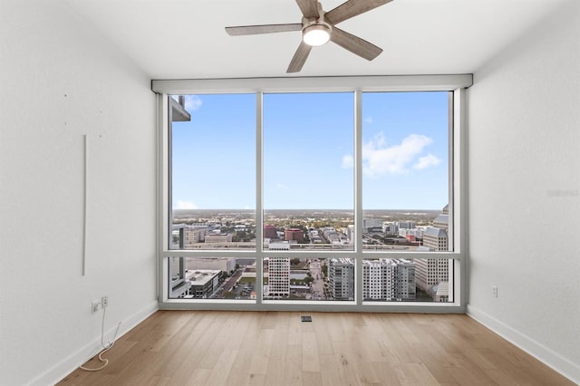 empty room featuring ceiling fan, expansive windows, and light wood-type flooring