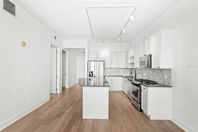 kitchen featuring white cabinetry, stainless steel appliances, backsplash, a kitchen island, and light wood-type flooring