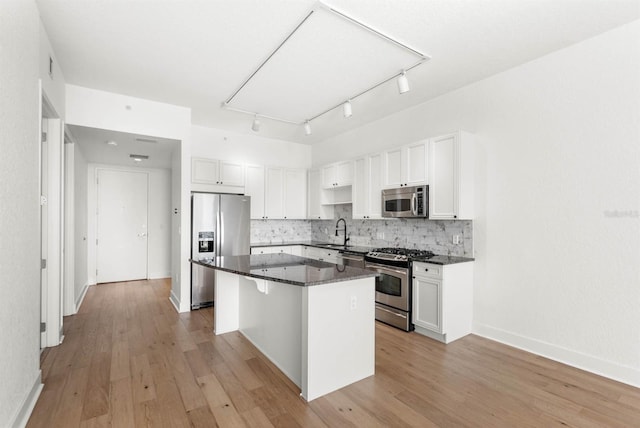 kitchen with a center island, backsplash, white cabinets, appliances with stainless steel finishes, and light hardwood / wood-style floors