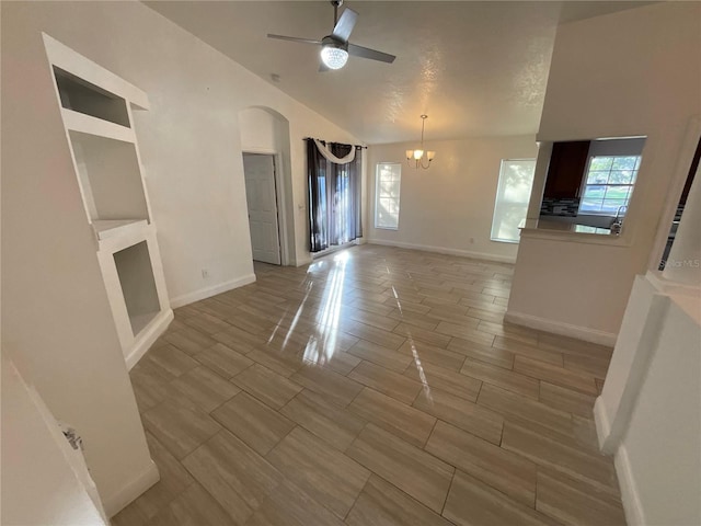 unfurnished living room with vaulted ceiling, a wealth of natural light, and ceiling fan with notable chandelier