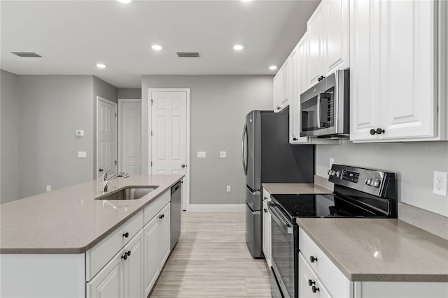 kitchen with a kitchen island with sink, sink, appliances with stainless steel finishes, light stone counters, and white cabinetry