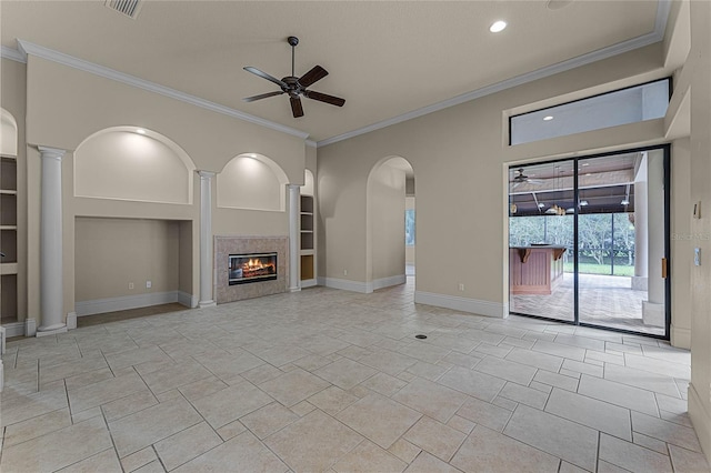 unfurnished living room featuring built in shelves, ceiling fan, ornate columns, a fireplace, and ornamental molding