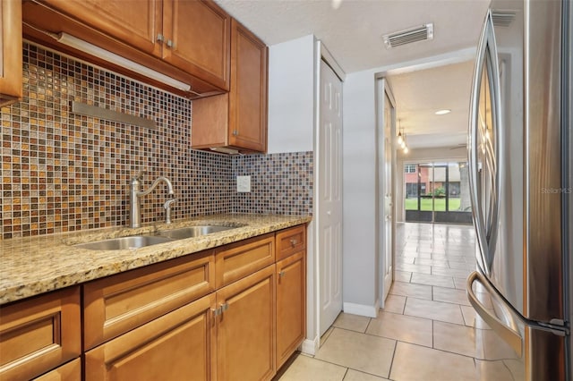 kitchen featuring light stone countertops, sink, tasteful backsplash, stainless steel fridge, and light tile patterned floors