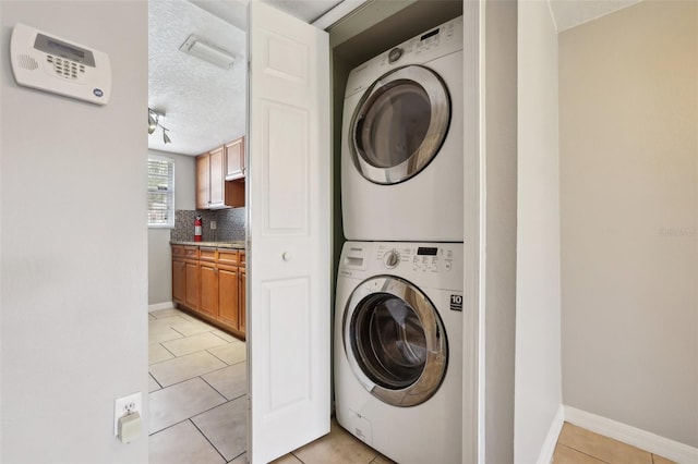 laundry area with stacked washer / dryer, light tile patterned flooring, and a textured ceiling