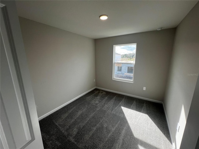 unfurnished room featuring dark colored carpet and baseboards