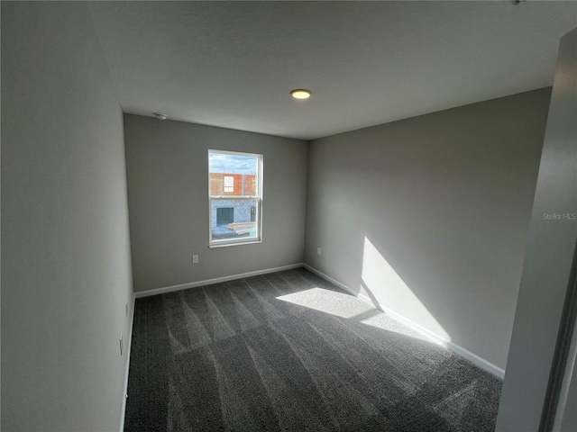 unfurnished room featuring dark colored carpet and baseboards