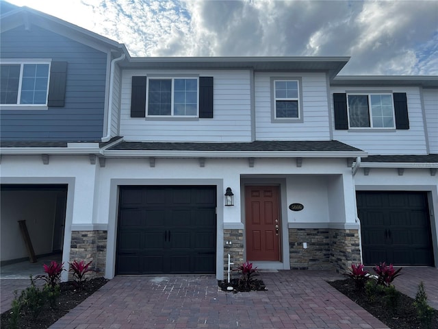 view of front facade featuring a garage, stone siding, a shingled roof, and driveway