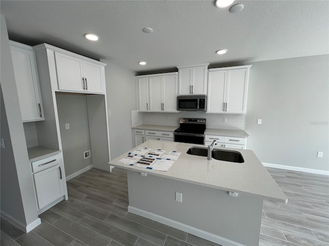 kitchen with stainless steel microwave, black range with electric stovetop, a sink, white cabinets, and an island with sink