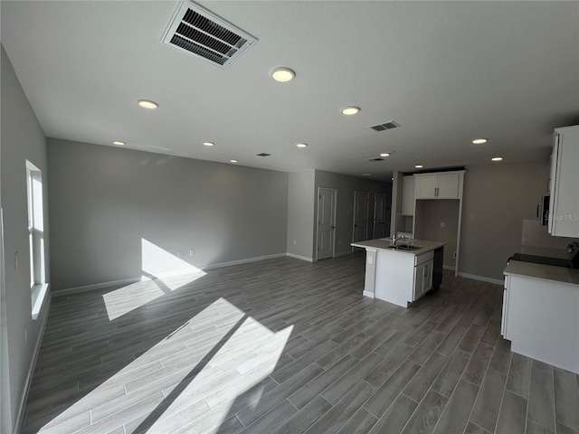 kitchen featuring a center island with sink, visible vents, dark countertops, white cabinetry, and a sink