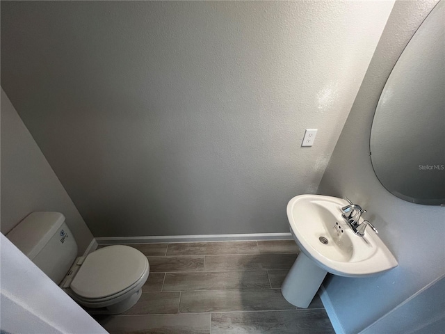 half bath featuring wood finish floors, baseboards, a sink, and toilet