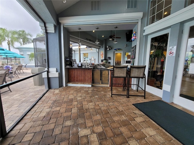 view of patio / terrace with ceiling fan, a bar, and glass enclosure