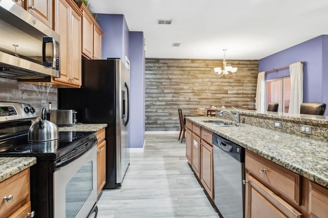 kitchen featuring light stone counters, stainless steel appliances, sink, hanging light fixtures, and wood walls