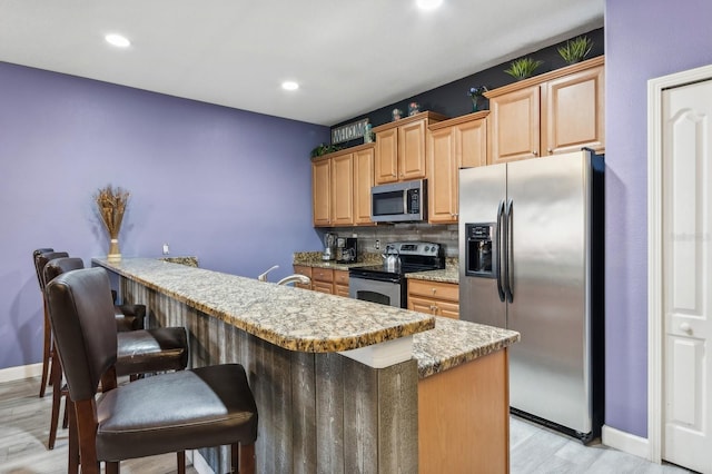 kitchen with appliances with stainless steel finishes, light wood-type flooring, tasteful backsplash, a kitchen breakfast bar, and sink