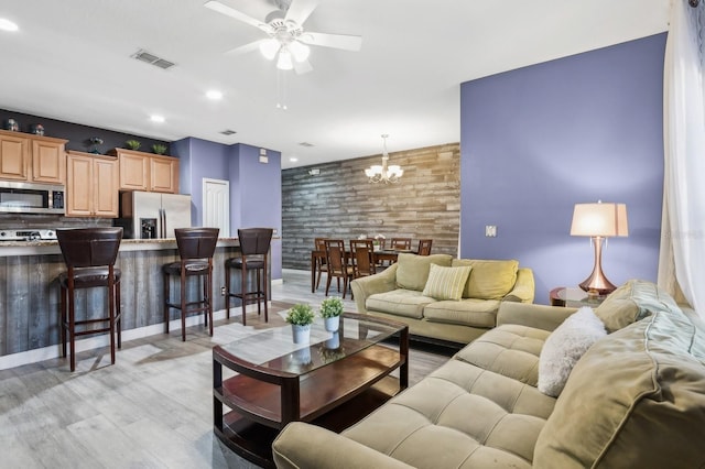 living room featuring ceiling fan with notable chandelier and light wood-type flooring