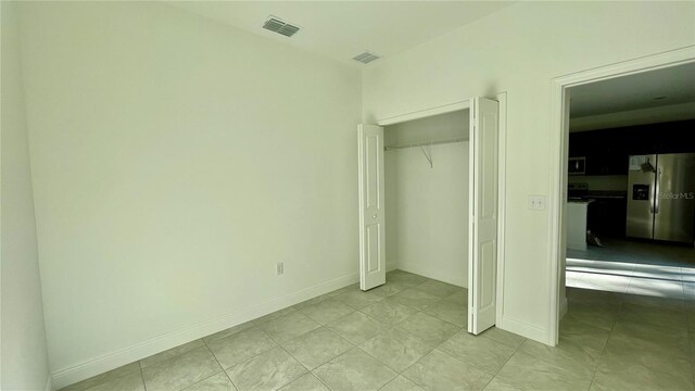 unfurnished bedroom featuring stainless steel fridge with ice dispenser, a closet, and light tile patterned floors