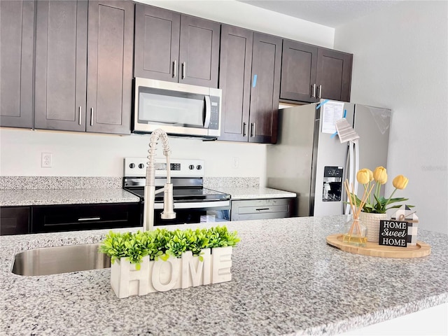 kitchen with light stone countertops, appliances with stainless steel finishes, and dark brown cabinetry