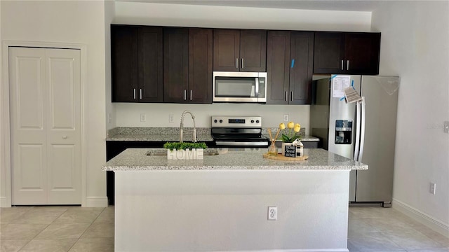 kitchen with dark brown cabinets, a kitchen island, light stone countertops, and appliances with stainless steel finishes