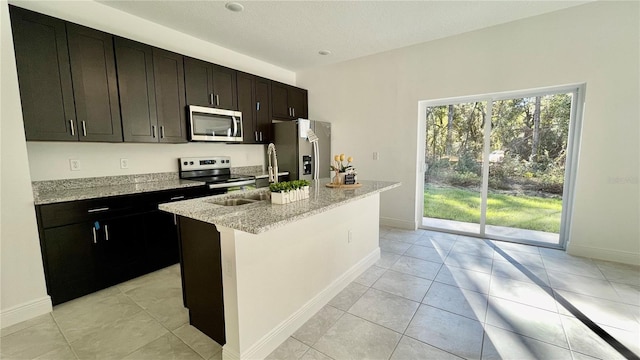 kitchen featuring a center island with sink, light stone counters, sink, and appliances with stainless steel finishes