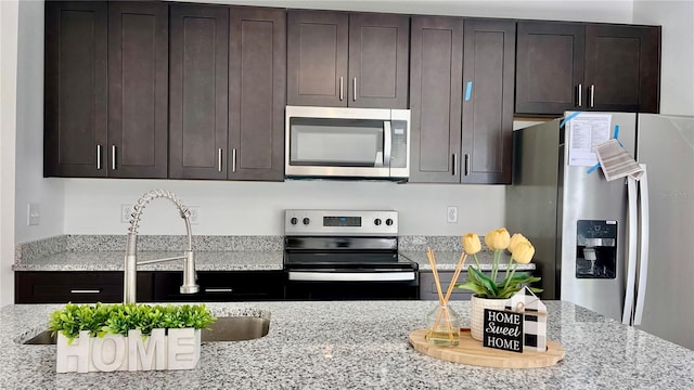 kitchen with dark brown cabinetry, light stone countertops, sink, and stainless steel appliances