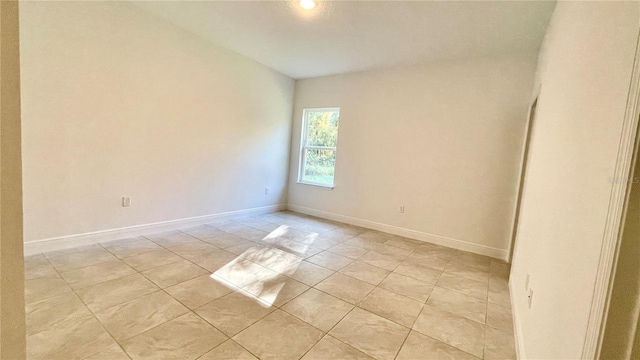 tiled empty room featuring lofted ceiling