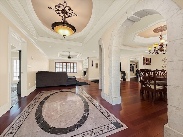 entrance foyer featuring ceiling fan with notable chandelier, a tray ceiling, crown molding, and dark wood-type flooring