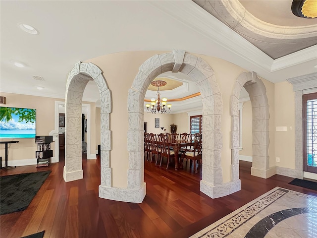 foyer with a raised ceiling, ornamental molding, dark hardwood / wood-style floors, and a notable chandelier