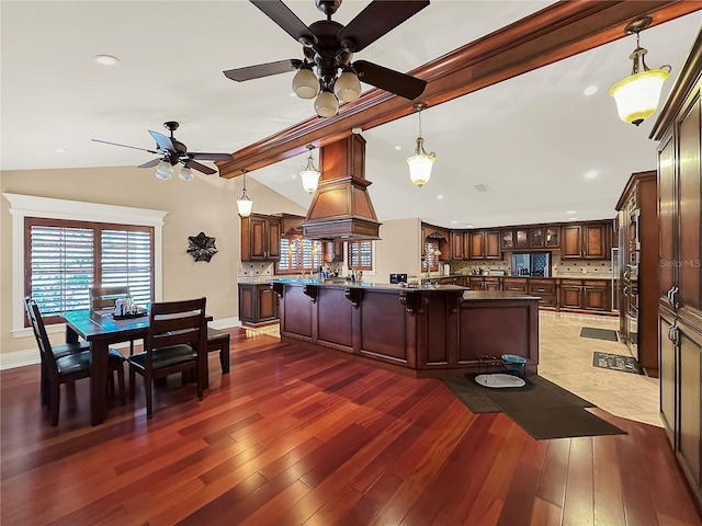 kitchen with ceiling fan, dark wood-type flooring, decorative light fixtures, vaulted ceiling with beams, and a breakfast bar area