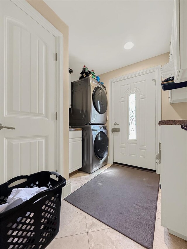 clothes washing area with stacked washer and dryer, light tile patterned flooring, and cabinets