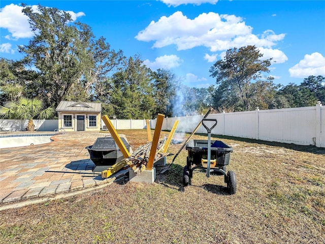 view of yard with an empty pool, a patio, an outdoor fire pit, and an outdoor structure