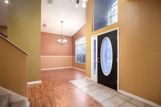 foyer with light wood-type flooring, high vaulted ceiling, and an inviting chandelier