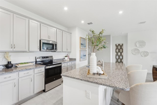 kitchen with a breakfast bar, light stone countertops, a center island with sink, and stainless steel appliances