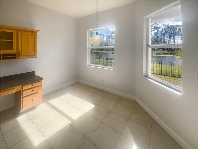 unfurnished dining area featuring a water view, built in desk, and light tile patterned floors