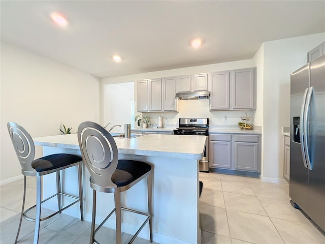 kitchen featuring gray cabinetry, a breakfast bar, stainless steel appliances, and an island with sink