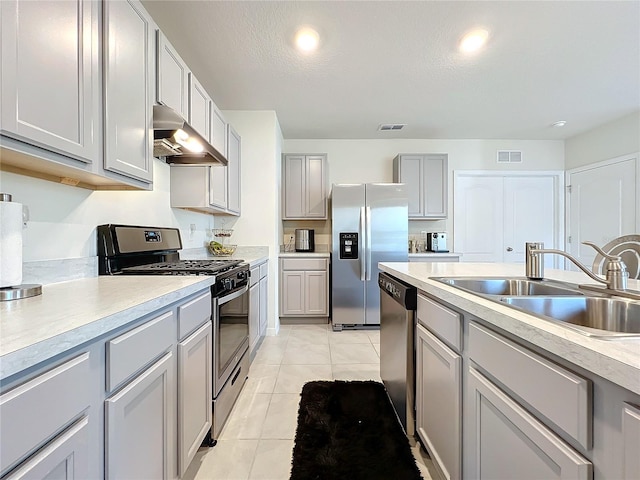 kitchen with a textured ceiling, stainless steel appliances, sink, light tile patterned floors, and gray cabinets