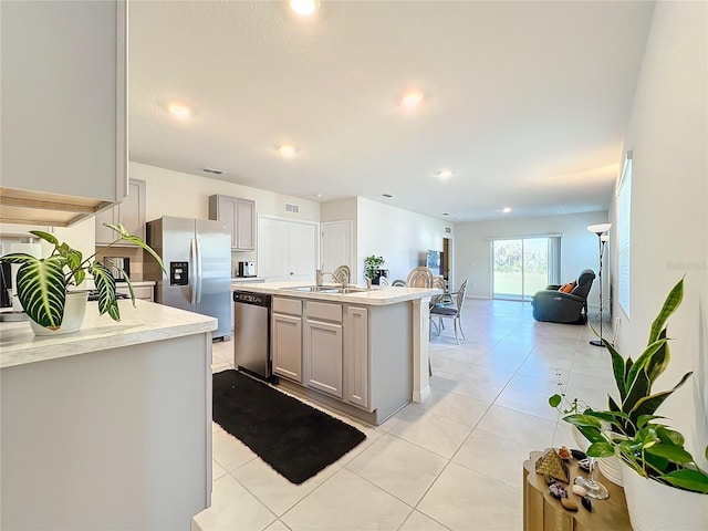 kitchen with gray cabinetry, sink, an island with sink, light tile patterned floors, and appliances with stainless steel finishes