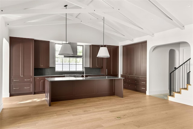 kitchen featuring hanging light fixtures, beamed ceiling, decorative backsplash, a center island with sink, and light wood-type flooring