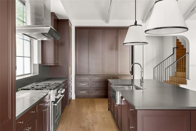 kitchen with double oven range, a center island with sink, wall chimney range hood, sink, and light hardwood / wood-style floors