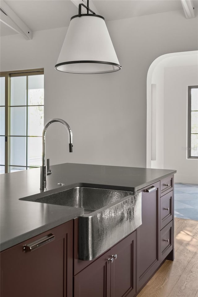 kitchen featuring beam ceiling, a healthy amount of sunlight, light wood-type flooring, and hanging light fixtures