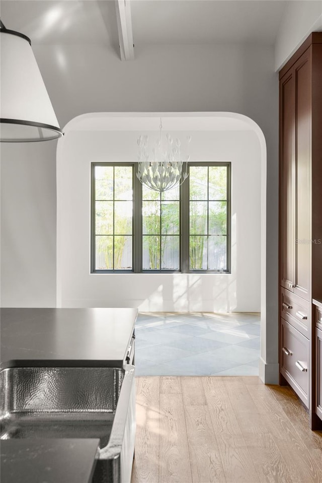 kitchen with lofted ceiling with beams, light hardwood / wood-style flooring, a healthy amount of sunlight, and a notable chandelier