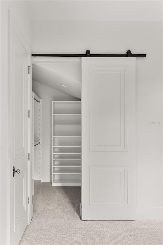 interior space featuring a barn door, lofted ceiling, and light carpet